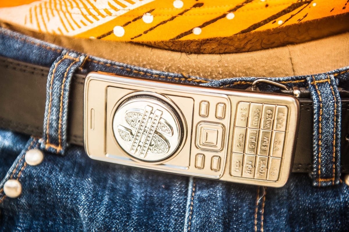 Untitled (Phone Buckle)  Image: Close up photograph of a phone-shaped buckle with a dollar sign on the screen.