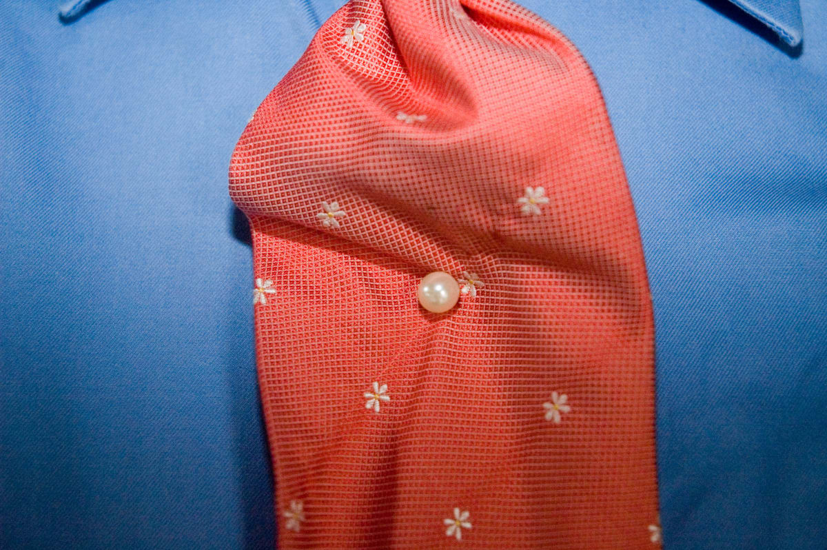 Untitled (Salvador Hassan getting dressed #5) by Daniele Tamagni  Image: Close up detail of Salvador Hassan's salmon tie with white flower embroideries and a pearl pin in it's center. Brazzaville, Congo (2007)