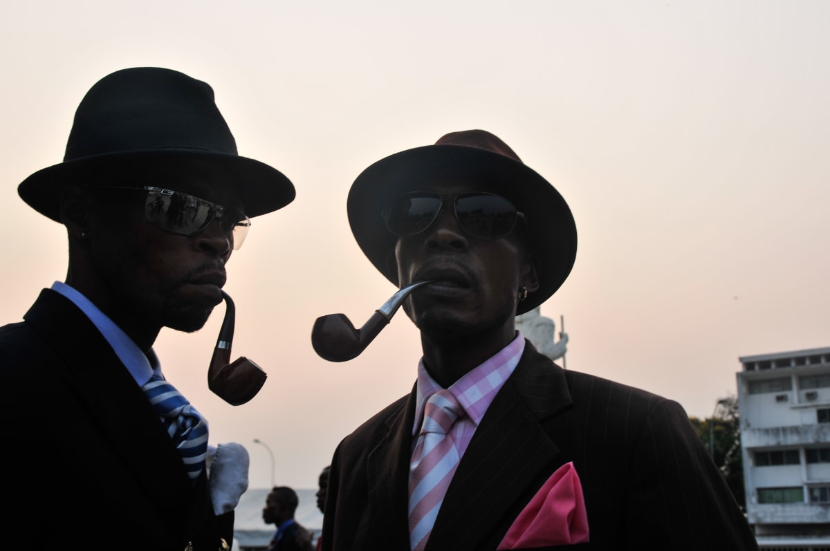 Untitled  Image: Two Sapeurs with black hats and dark sunglasses holding pipes between their teeth. Brazzaville, Congo (2008)