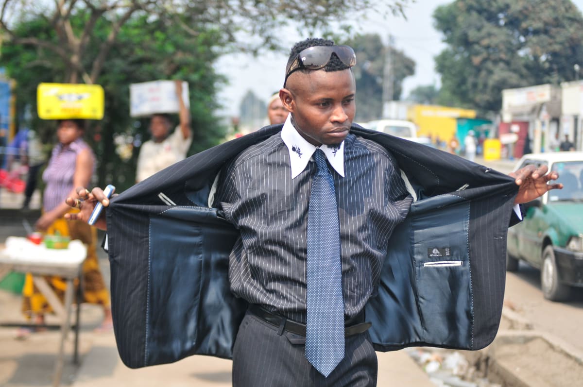 Untitled  Image: Sapeur showing off his blue and white pinstriped outfit by opening his jacket. Brazzaville, Congo (2008)