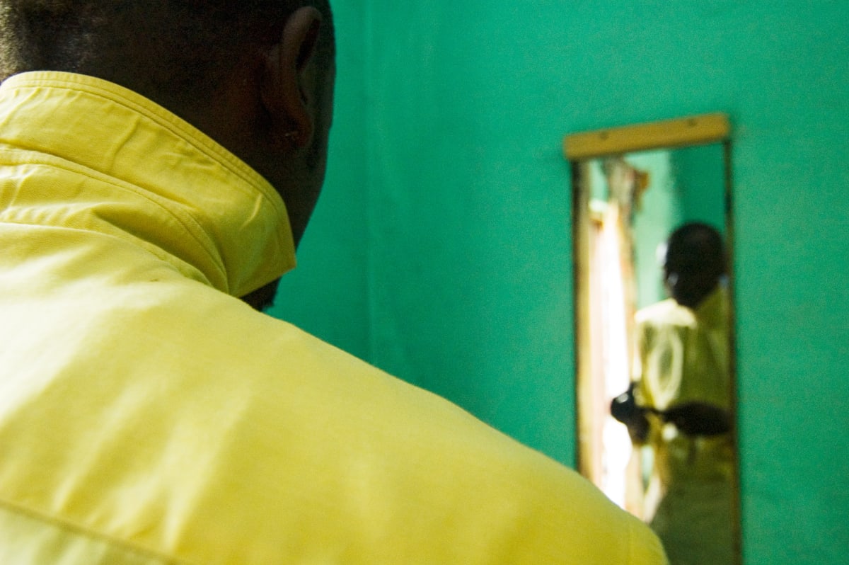 Untitled  Image: Photograph of Lalhande taken from behind, wearing a yellow shirt. Out of focus, in the background, his reflection in the mirror hanging on a green wall. Brazzaville, Congo (2007)