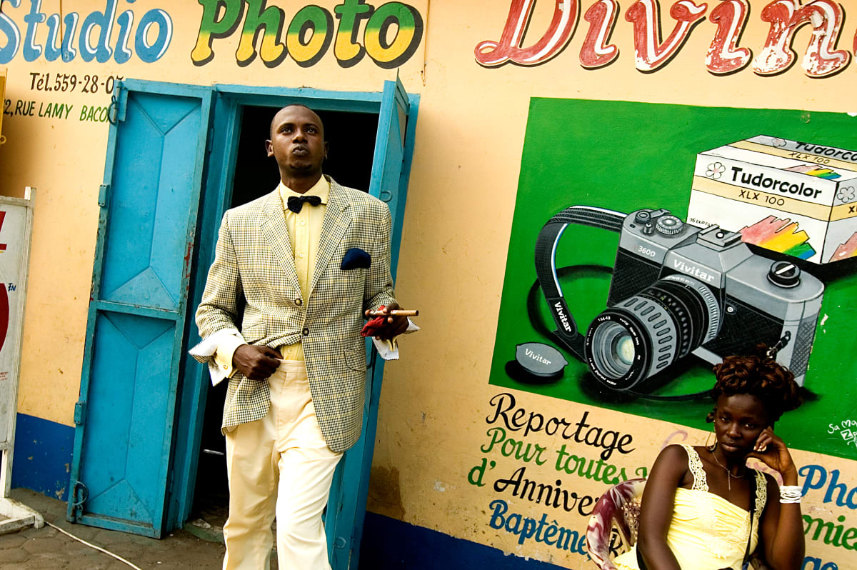 Untitled (Lalhande in front of the photostudio)  Image: Lalhande in front of a photography studio, wearing a tweed jacket and yellow trousers and shirt, holding a cigar in his left hand. Brazzaville (Congo), 2007

From 'Gentlemen of Bacongo'