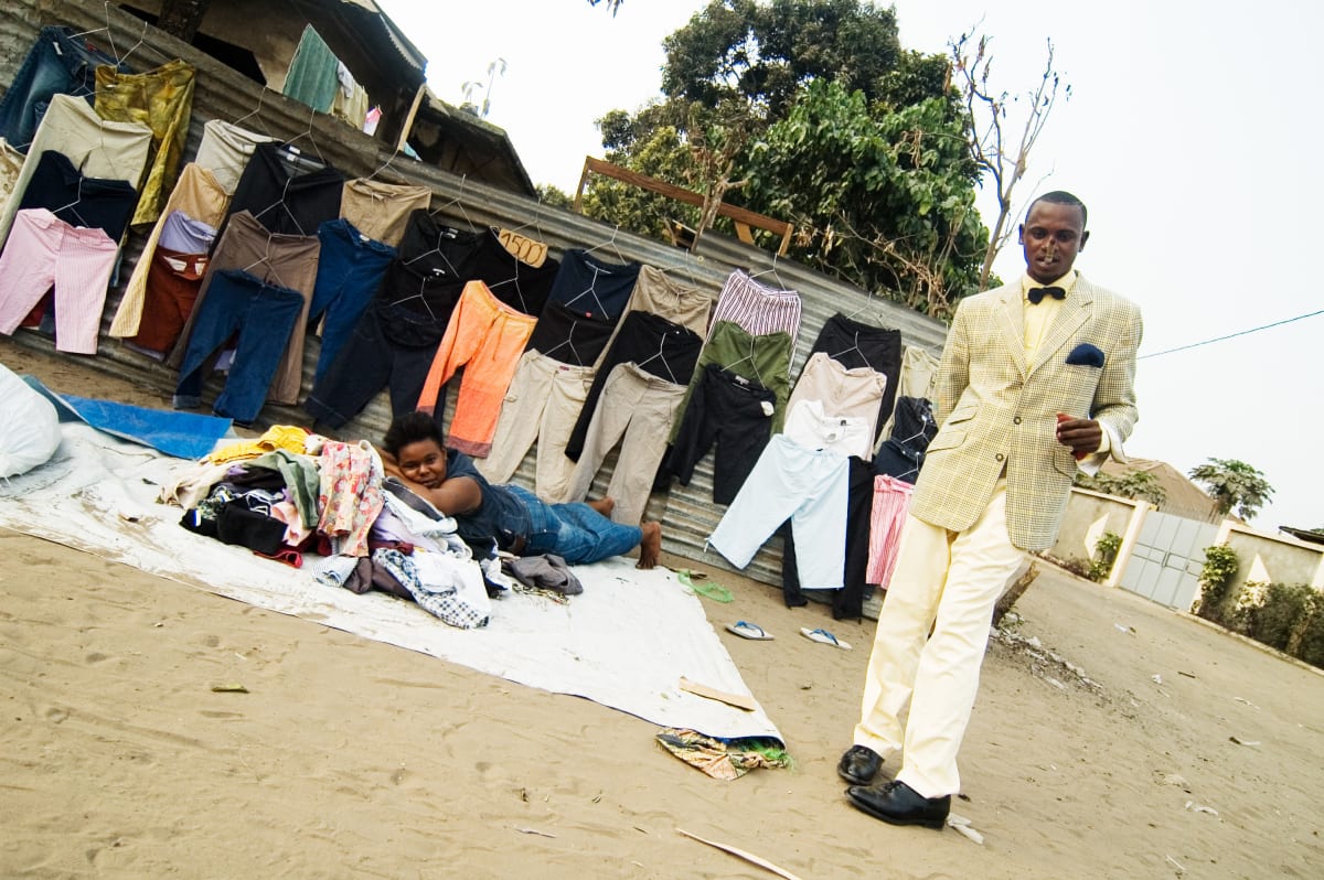 Untitled by Daniele Tamagni Foundation  Image: Lalhande posing for the camera on the streets of Brazzaville, standing before a clothes stall. Brazzaville, Congo (2007)