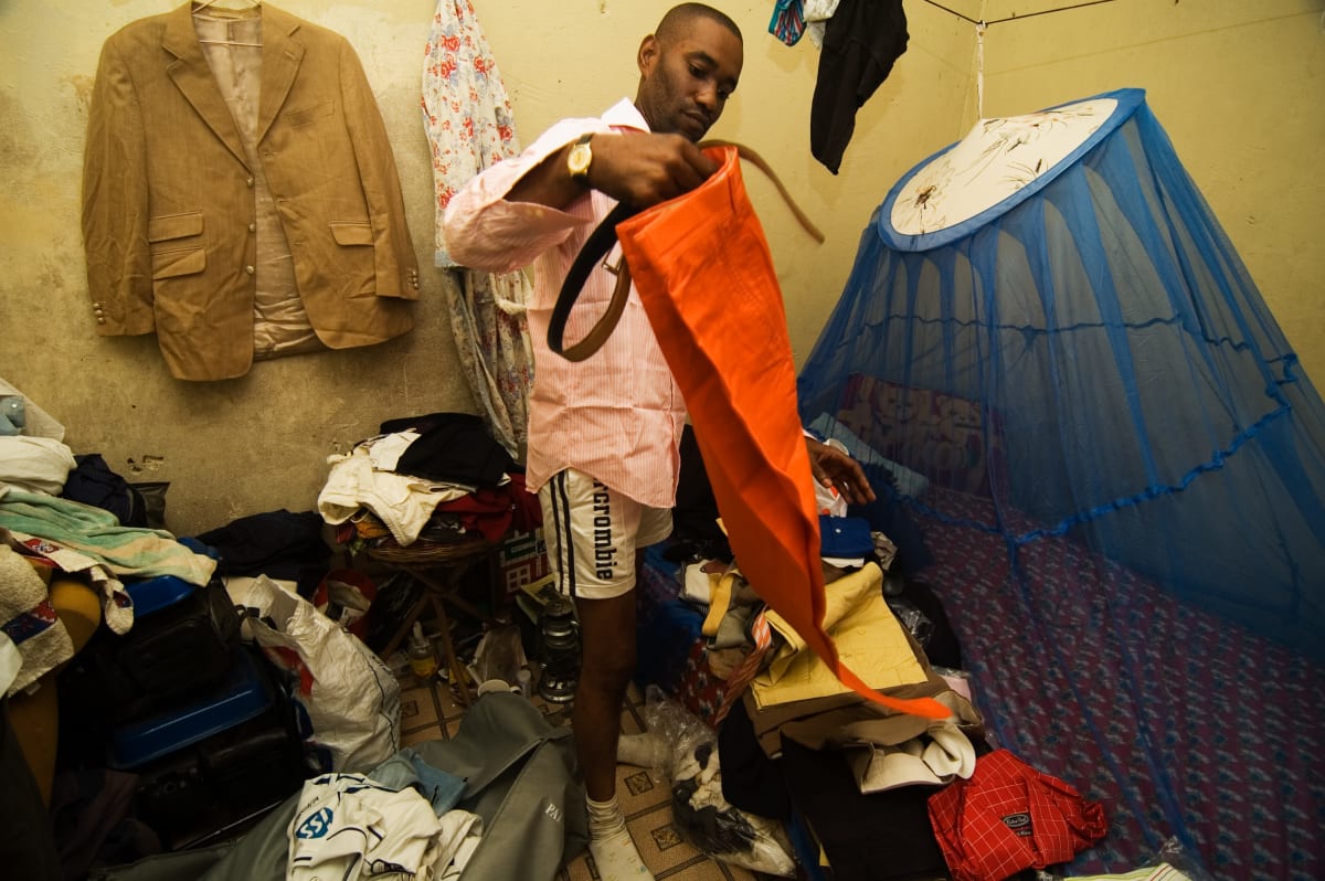 Untitled by Daniele Tamagni Foundation  Image: Arca in his bedroom holding the orange trousers of his suit. Brazzaville, Congo (2007).