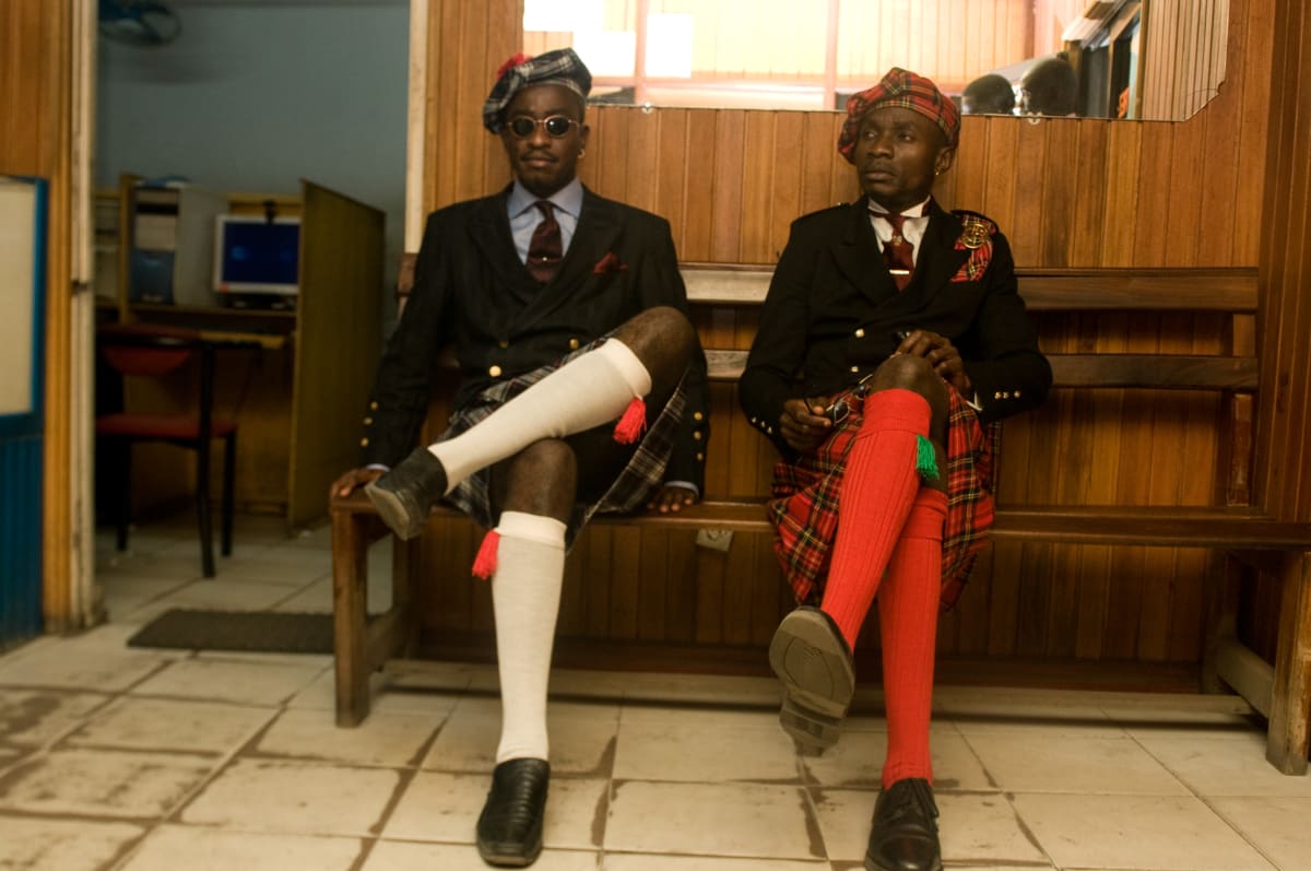 Untitled (The Piccadilly Group) by Daniele Tamagni Foundation  Image: Two members of the Piccadilly Group sitting on a wooden bench, wearing a kilt. Brazzaville, Congo (2008)