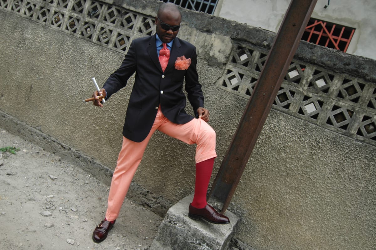Untitled by Daniele Tamagni Foundation  Image: Salvador Hassan showing off his red socks and leather shoes  whilst holding two cigars in his right hand, in the streets of Brazzaville, Congo (2007)