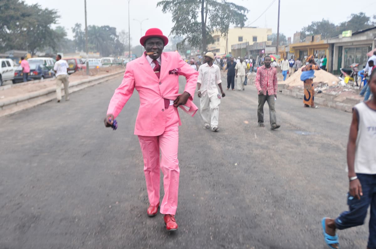 Untitled (Willy Covary) by Daniele Tamagni Foundation  Image: Willy Covary in his dashing pink suit and red bowler hat, tie and shoes walking down the streets of Brazzaville, Congo (2008).