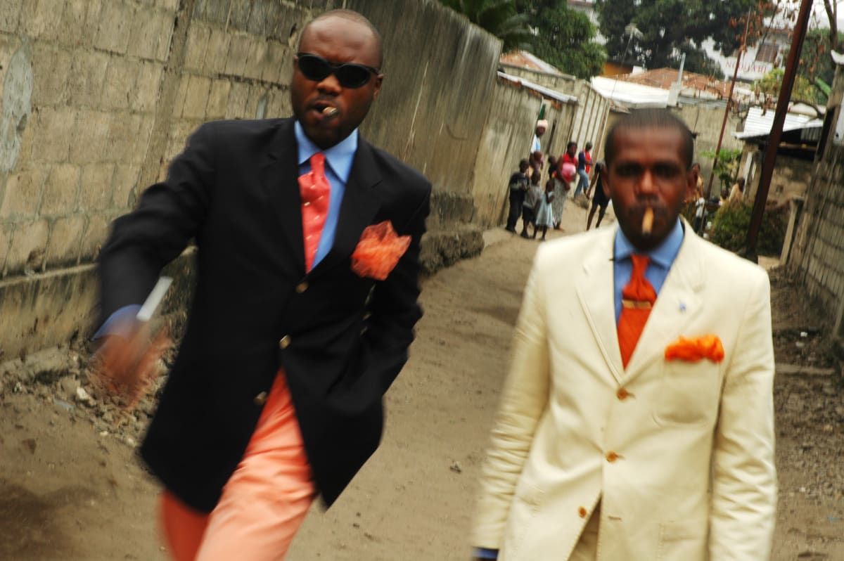 Untitled  Image: Salvador Hassan (left) walking in a street of the Poto Poto district with his friend Phael. Salvador is the former leader of the 'Piccadilly Group', one of the most innovative groups in the Sape landscape. He works for MTN, a mobile company, and as 'vestimentaire' advisor, helping people in their purchase of suits. Brazzaville, Congo (2007)