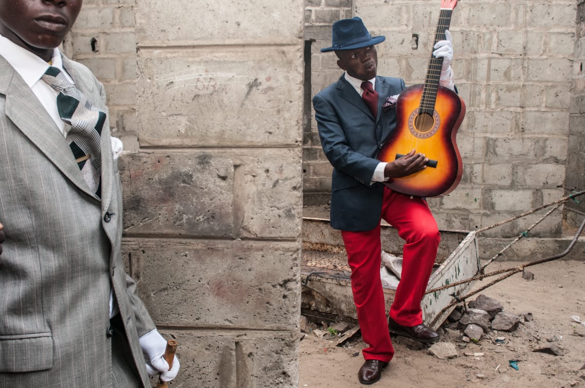 Untitled by Daniele Tamagni Foundation  Image: Two young Sapeurs, one in a grey suit and the other posing with his guitar. Brazzaville, Congo (2008)