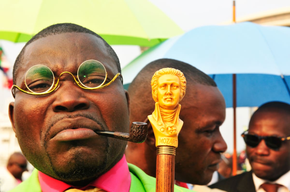 Untitled (Eric Massakampa at Rapha Bounzeki party)  Image: Portrait of the Sapeur Eric Massakampa with a pipe between his lips, holding next to his face the handle of his cane, carved to represent the portrait of Mozart. Brazzaville, Congo (2008)