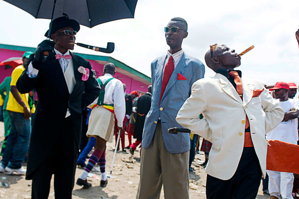 Untitled (Lamame and Sapeurs)  Image: Lamame (left) standing next to two Sapeurs, one of which is holding an unlit cigar between his teeth. Brazzaville, Congo (2008)
