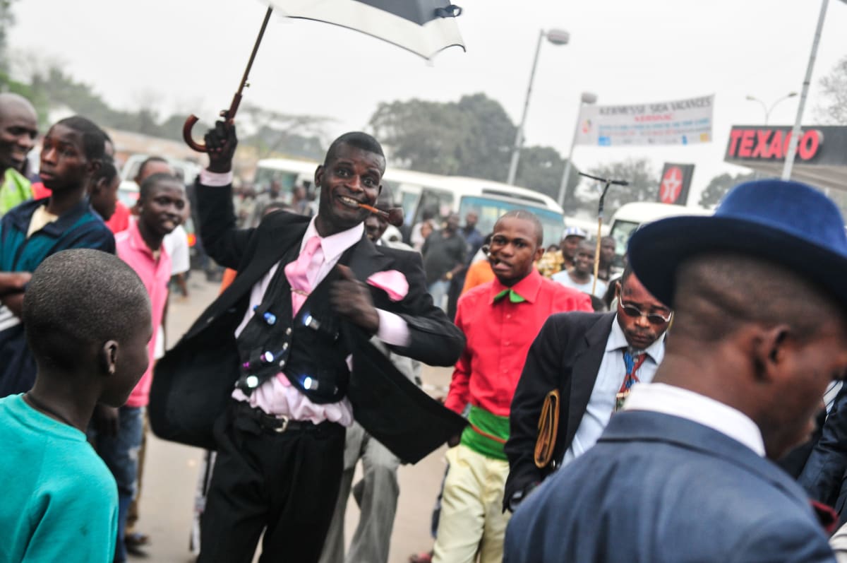 Untitled (Christian Malala with Umbrella)  Image: Sapeur Christian Malala with open umbrella performing on the street. On his jacket, five torches. He is wearing a black suit with pink shirt, tie and pocket handkerchief. Brazzaville, Congo (2008)