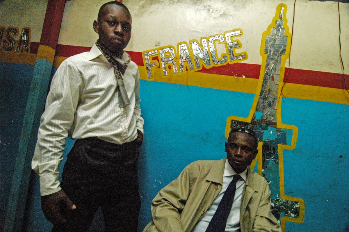 Untitled  Image: Lalhande (right) with a friend sitting in front of a mirror shaped as the Eiffel Tower. Paris is the historical dream of every Sapeur: the capital of fashion that everyone wishes to visit. Brazzaville, Congo (2007)