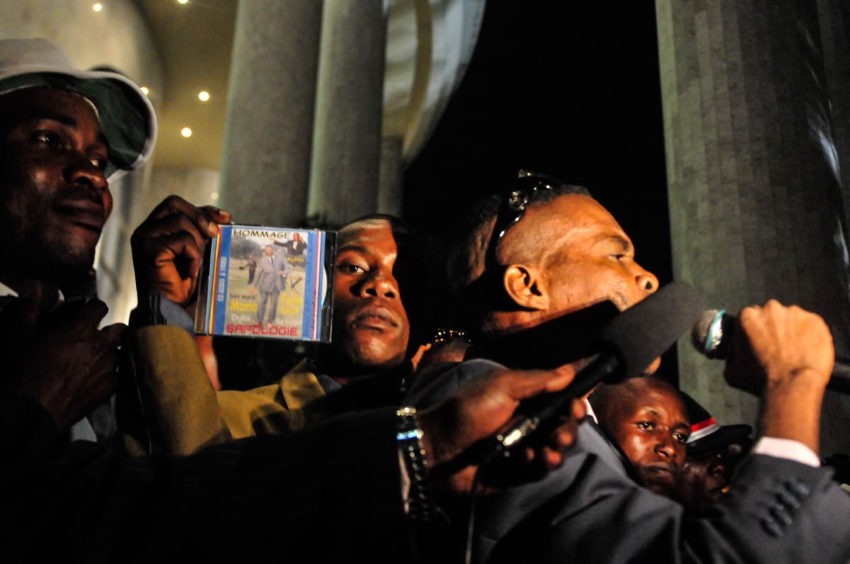 Untitled  Image: Night scene from a party with Rapha Bounzeki, musician who 'sings' Sape. Music which talks about Sape is the wordcarrier of Sape - Rapha limits himself to sing about Sape without the presumtion to influence or teach the Sapeurs. In the center of the picture, a man holding a cd entitled 'Sapologie'. Brazzaville, Congo (2008)