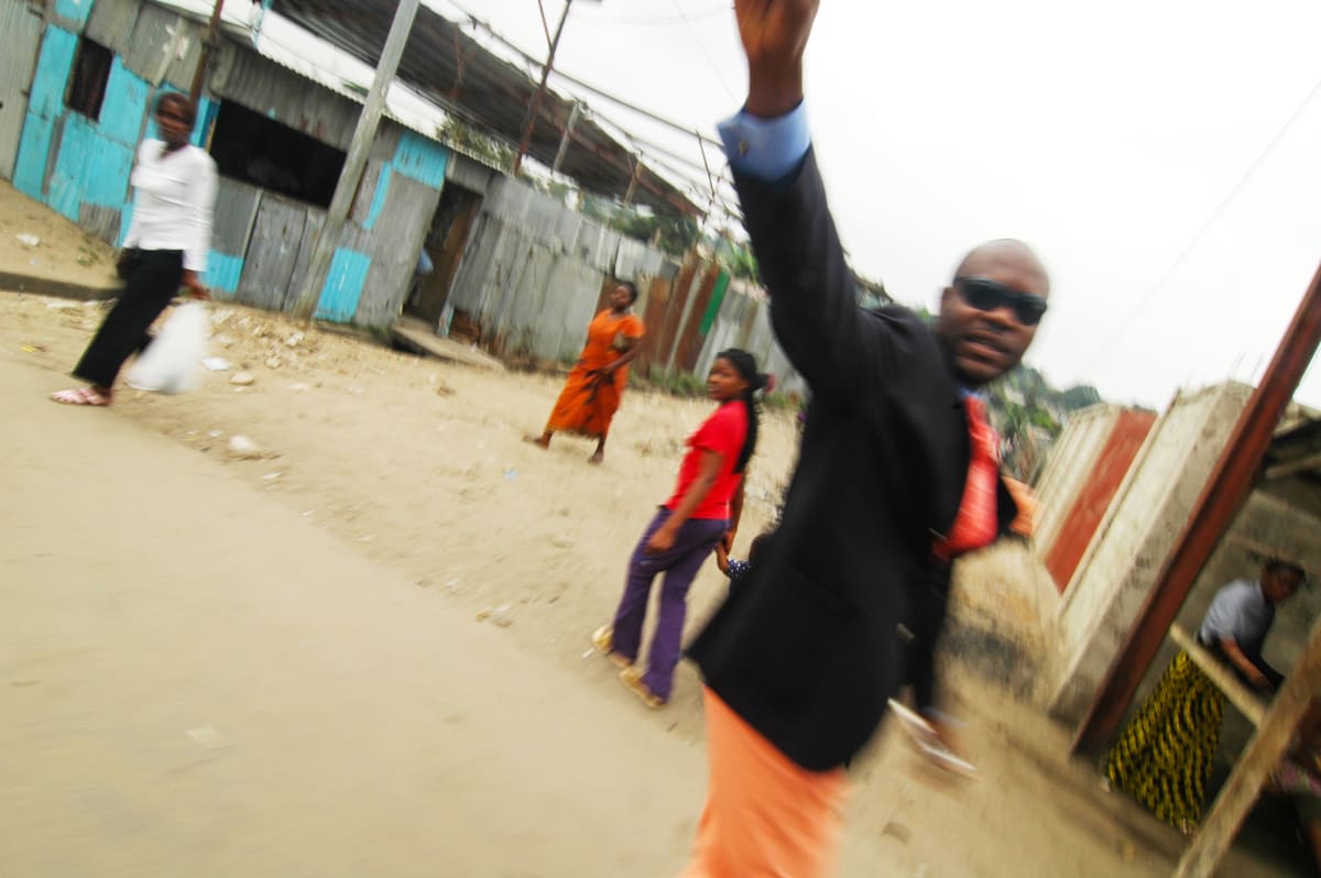 Untitled by Daniele Tamagni Foundation  Image: Salvador Hassan waving his right arm whilst passing through a street in Poto Poto distric, Brazzaville, Congo (2007).