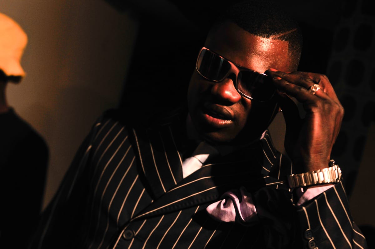 Untitled  Image: Portrait of a Sapeur with dark sunglasses at a nightclub, wearing a black and white pinstripe suit and a lilac pocket handkerchief. Brazzaville, Congo (2008)