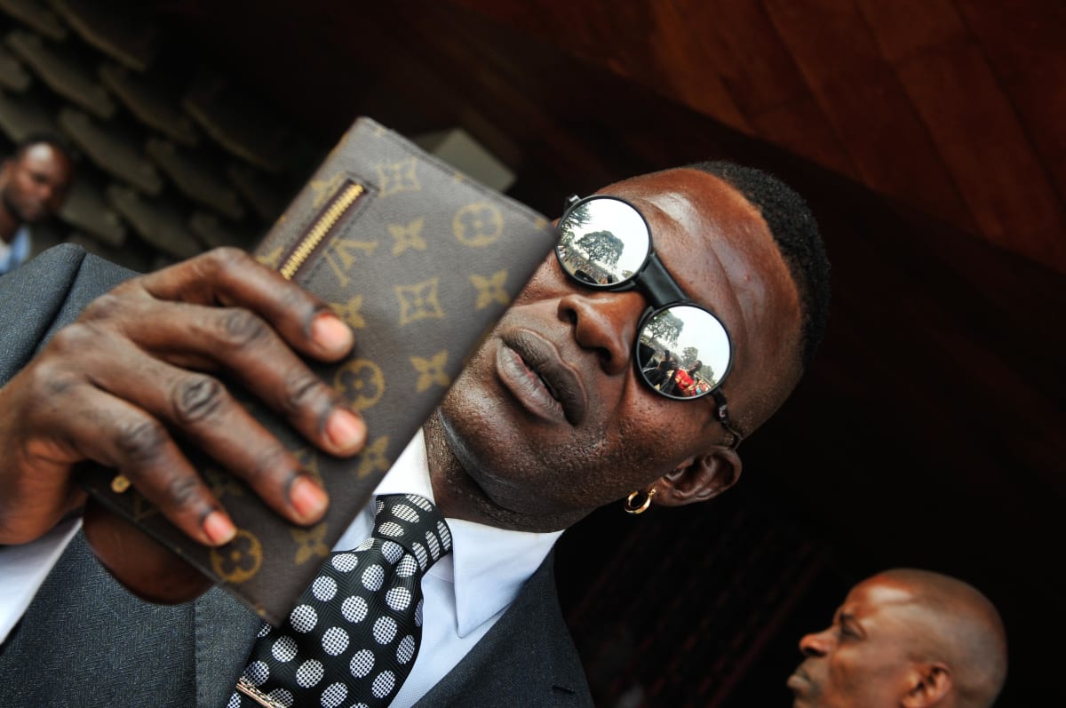 Untitled  Image: Portrait of a Sapeur holding a Louis Vuitton wallet, wearing sunglasses and a polkadot tie. Brazzaville, Congo (2008)