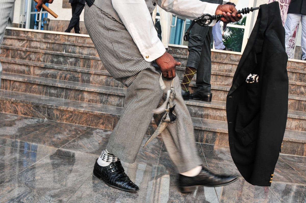 Untitled  Image: A sapeur performing for the camera, holding his jacket on the handle of a black, carved stick in one hand and his bowtie in the other. Brazzaville, Congo (2008)