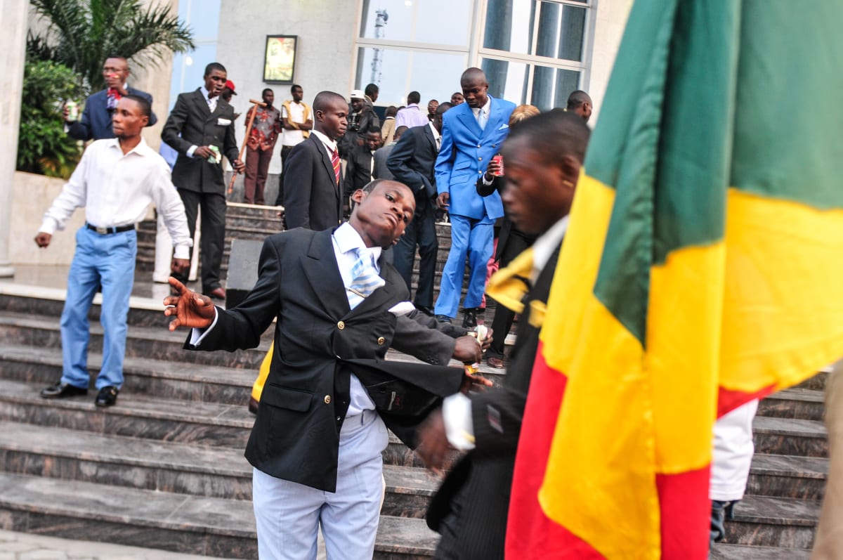 Untitled  Image: A Sapeur performing amidst a group at a party, whilst a man holding the Congolese flag is passing by. Brazzaville, Congo (2008)