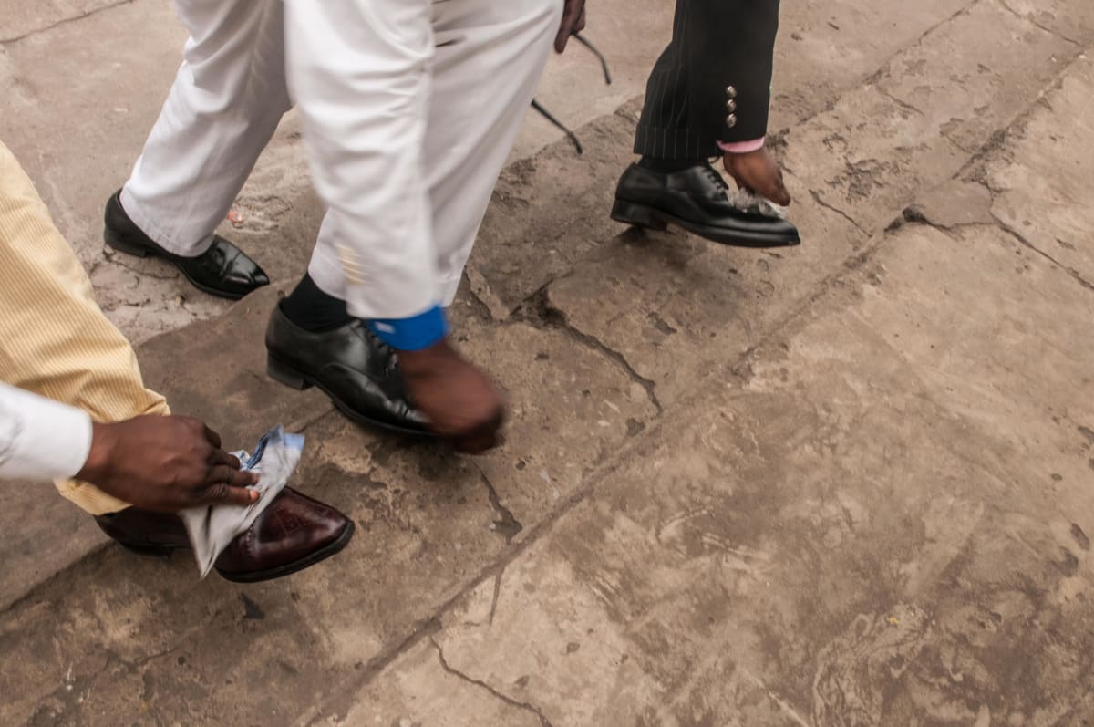 Untitled  Image: Close up photograph of Mayembo, Dany Blaise and a friend polishing their leather shoes on a sidewalk during a walk in the city. Brazzaville, Congo (2008)