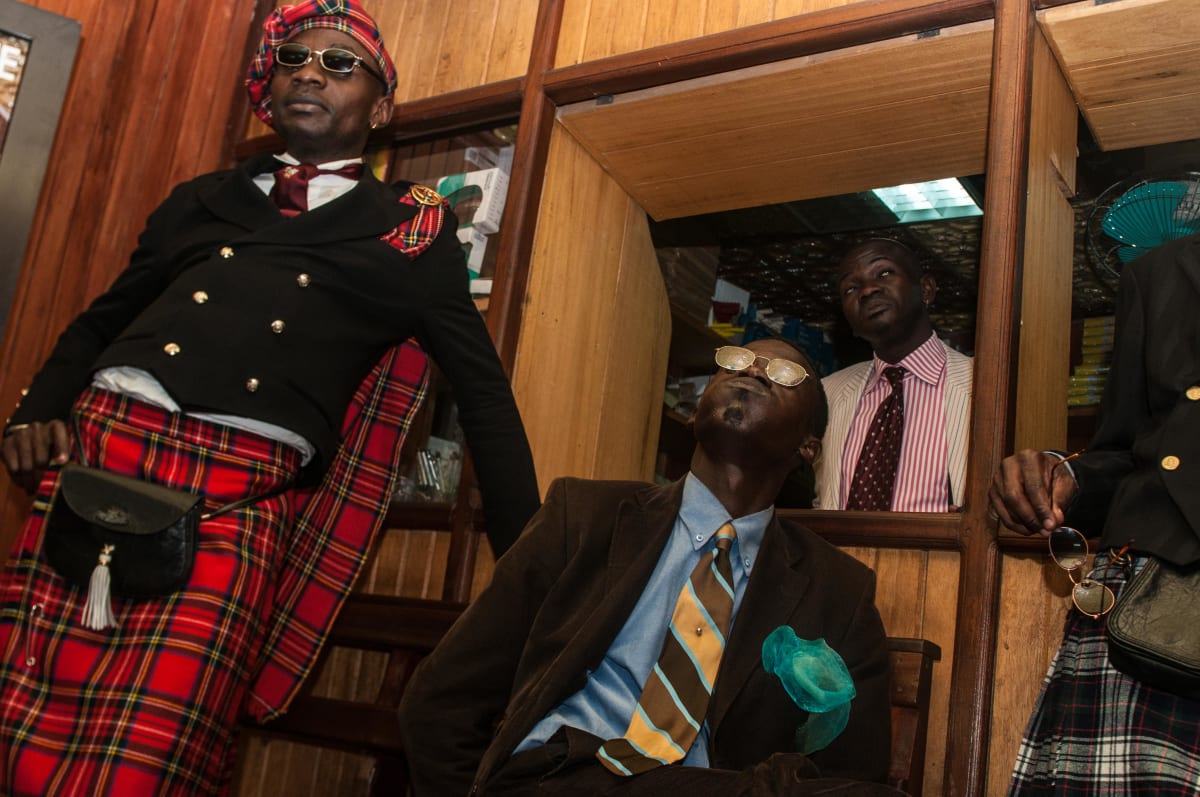 Untitled by Daniele Tamagni Foundation  Image: Two members of the Piccadilly group hanging out in a friend's shop with other Sapeurs. Brazzaville, Congo (2008)