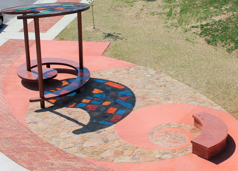 Learning Curve by Lynn Basa  Image: Learning Curve honors the past of this small Appalachian town as one of the country’s leading producers of brick and aggregate as well as the world headquarters of Eastman Chemical. The canopy is a map of the 1906 “City Beautiful” town plan and was fabricated by a local sculptor, John Robinson at Appalachian Ironworks. The inset material is “Tritan”, a newly-invented monomer donated by Eastman Chemical. The recycled brick is from a demolished paper plant, another former industry once important to the town.   A local concrete worker and mason did the stonework.