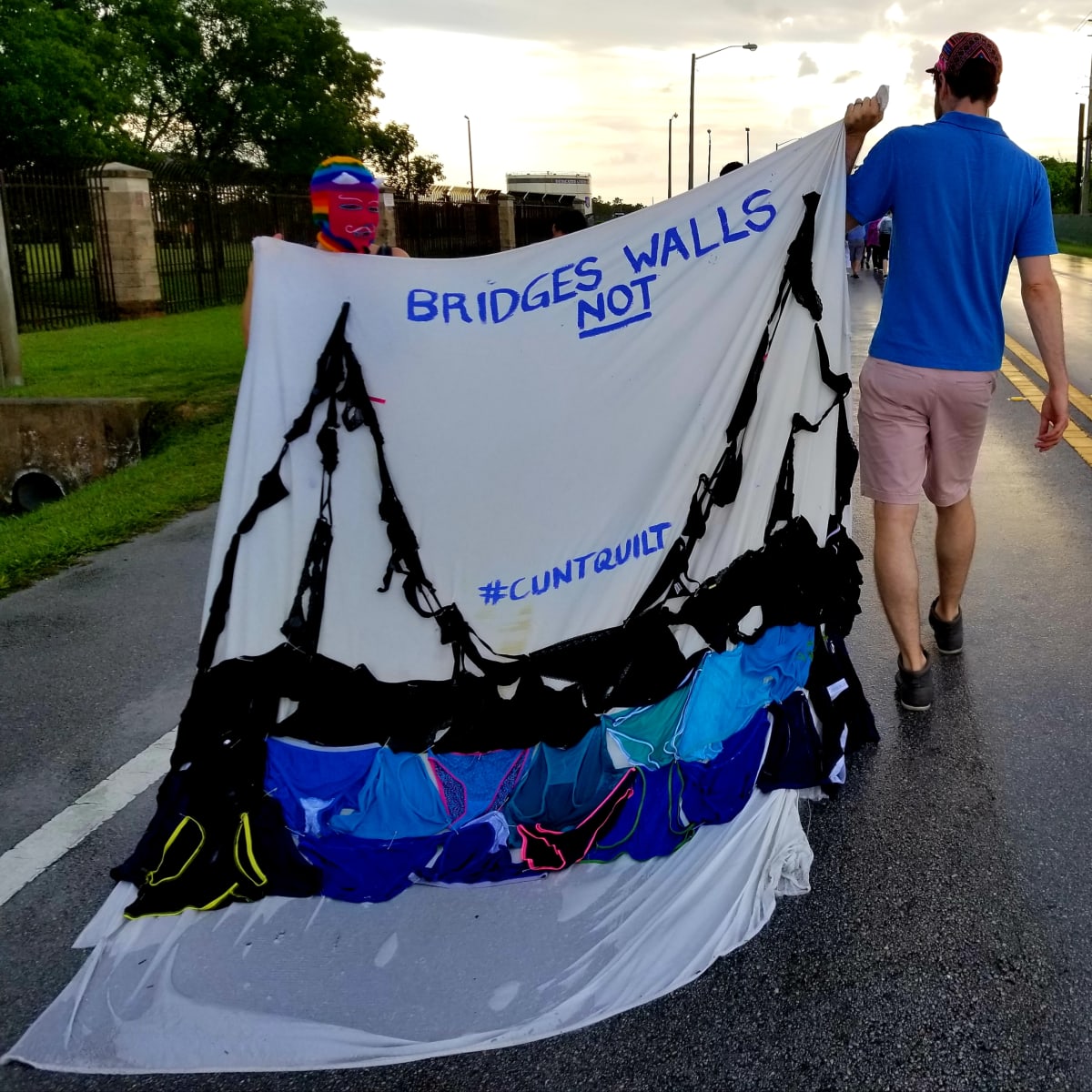 Arpillera Americanx * Cunt Quilt (Bridges) Cunt Congress by Coralina Rodriguez Meyer  Image: Artist Coralina Rodriguez Meyer and her partner bear Arpillera Americanx * Cunt Quilt (Bridges) during in a Performance of Citizenship at the March to Keep Families Together Cunt Congress on June 23, 2018 a mile from the artist's childhood home where children separated from their families are incarcerated by the US government. 