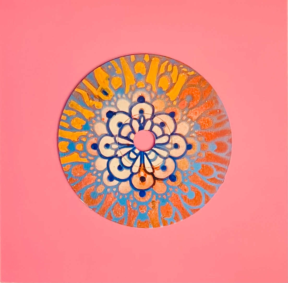 Sunburst Mandala by Dr. Vasundhara (Vasu) Tolia  Image: A cheerful mandala with a central flower motif surrounded by
radiating sunburst patterns in warm oranges, blues, and yellows on a coral pink background.