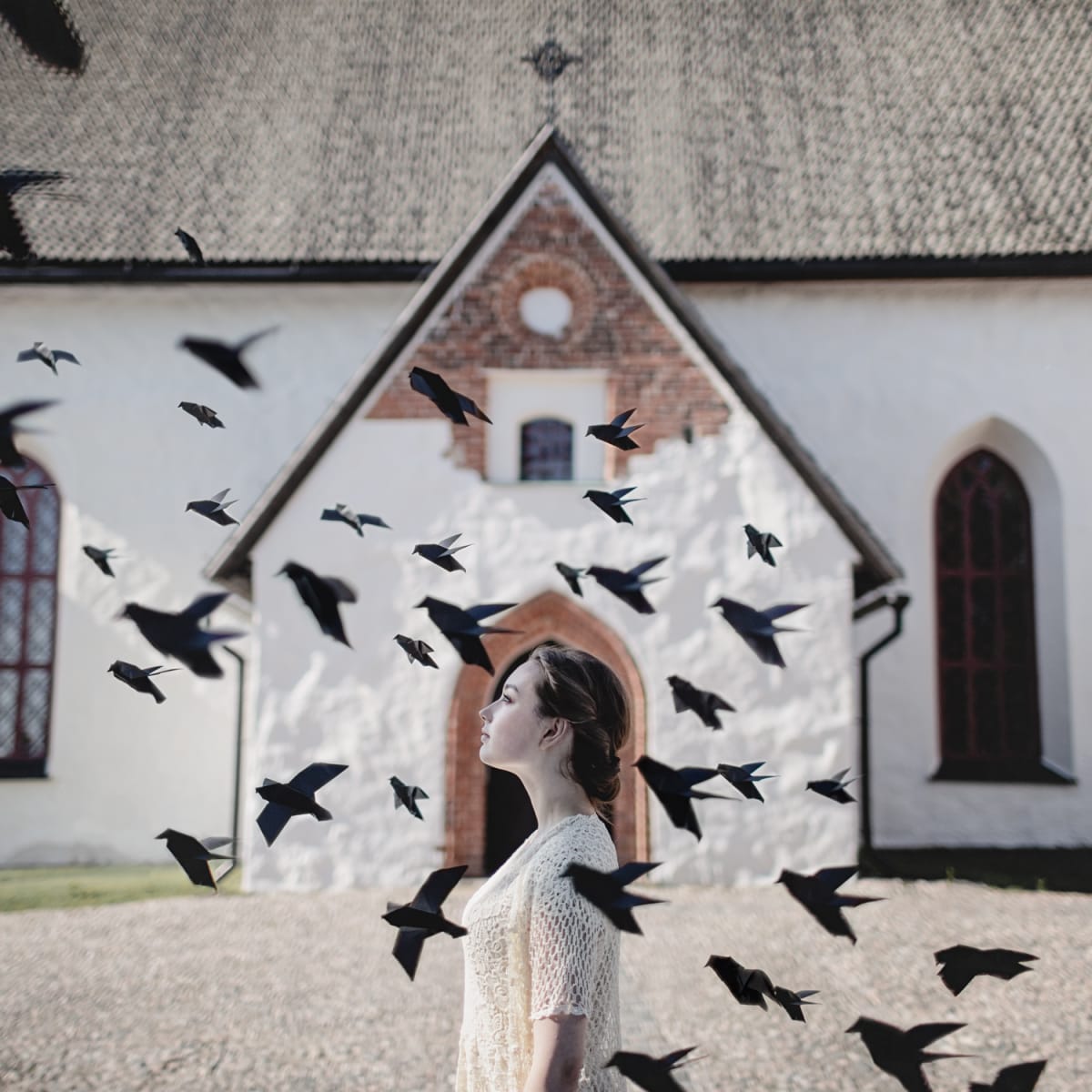 I Have Wings Too by Dasha Pears  Image: This work is a part of the project shot in collaboration with the tourist board of Old Porvoo, one of the most charming little towns in Finland. In the project, we were telling a story of a girl, who lives in Porvoo and places that are special to her, like the ancient church that you can see behind her in this image. The black origami birds symbolize dreams, hope, and the sense of freedom that her heart is filled with right now. In addition, real blackbirds flying around the church are a part of this major sight of Porvoo, they are always there, kind of like pigeons at the main square of Venice and people come to watch them all the time.