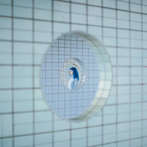Tunnel by Dasha Pears  Image: This work came along when I was shooting my Paper Cuts project, focused above all on monochrome, of the color blue in this case. It was shot at a commuter train station in Helsinki, Finland, and takes advantage of its unique design.
When I saw those round windows I immediately thought of 2 things:
1) they reminded me of a portal of some kind, a portal to a parallel world, the world of our imagination
2) the shape, when viewed from the side became oval and became a classic oval portrait frame, perhaps 200 years ago a person could carry a small portrait like that on his or her neck in a locket.
That could be a portrait of someone near and dear.
I thought in this case it might be a portrait or an image of a better self, the one perhaps you're striving to become.