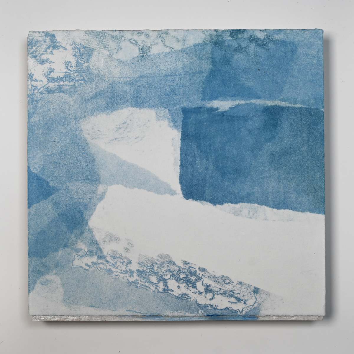Ice Watch Studies #29 by Megan Broughton  Image: A series of experimental etchings evoking atmospheric Arctic seascapes. These pieces were made in memory of ice watches during the MaréMotrice artist residency in Greenland, sailing through foggy fjords. They function like a brilliant, shapeshifting, reveal through the fog and play with Arctic mirages and cause tricks of the eye. There are moments of clear detail and sublime wonder amidst fragmentation. Two etching plates were printed over each other multiple times in different orientations to create new and abstracted imagery. Stencils made of torn newsprint were used to block ink during the printing process, creating the white shapes throughout the works. The stencils were continually torn apart and reused throughout the series so that the stencil shapes become self-referential but are constantly transforming and deteriorating. Mounted on a cradled wooden panel.