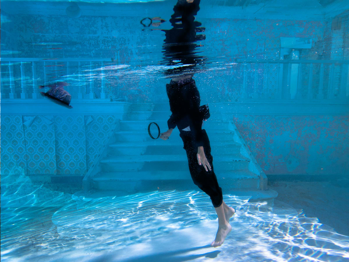 Beneath the Surface 15  Image: Mixed media photograph of young male teen in suit underwater in abandoned room with magnifying glass and fedora.