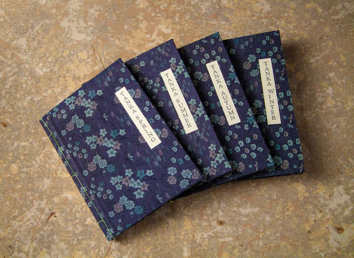 TANKA YEAR by George Roberts  Image: Japanese style Tanka poetry, set in Japanese style stab binding Edo period book form.  Each of the four books contains thirty-one poems on its given season, printed on mulberry papr.  Covers made from silk kimono cloth.  Edition of seven.