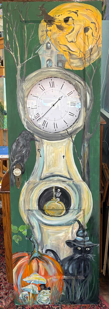 The Midnight Watch by Amy B. Carroll  Image: A whimsical Halloween-themed painting on a vintage door transformed into a working clock. Under a glowing moon, a witch flies above a crooked tower while a raven, a hat-wearing black cat, and a jaunty toad gather around a pumpkin below. A tiny skeleton swings from the pendulum, adding playful magic to this upcycled, storybook-style piece.