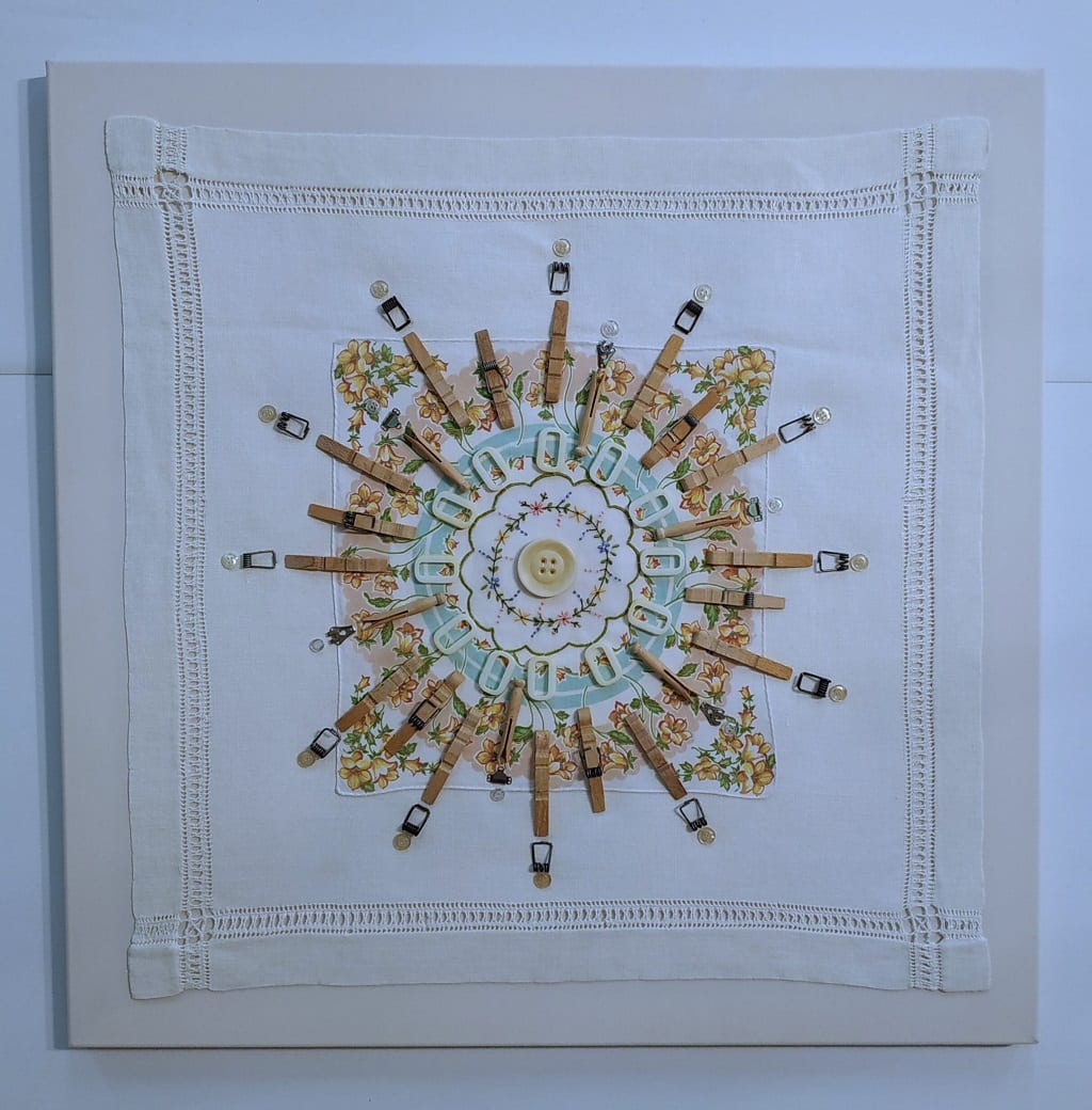 Laundry Mantra: Off the Peg by Lesley Turner  Image: Lesley Turner, 'Laundry Mantra: Off the Peg', 2021, 28" x 28". Vintage cotton domestic linens, metal, and wood pegs, plastic rings, buttons, and polyester thread. A laundry mantra represented by a mandala is repeatedly uttered to keep the mind and body focused on a demanding repetitive task that also requires great attention to detail.
