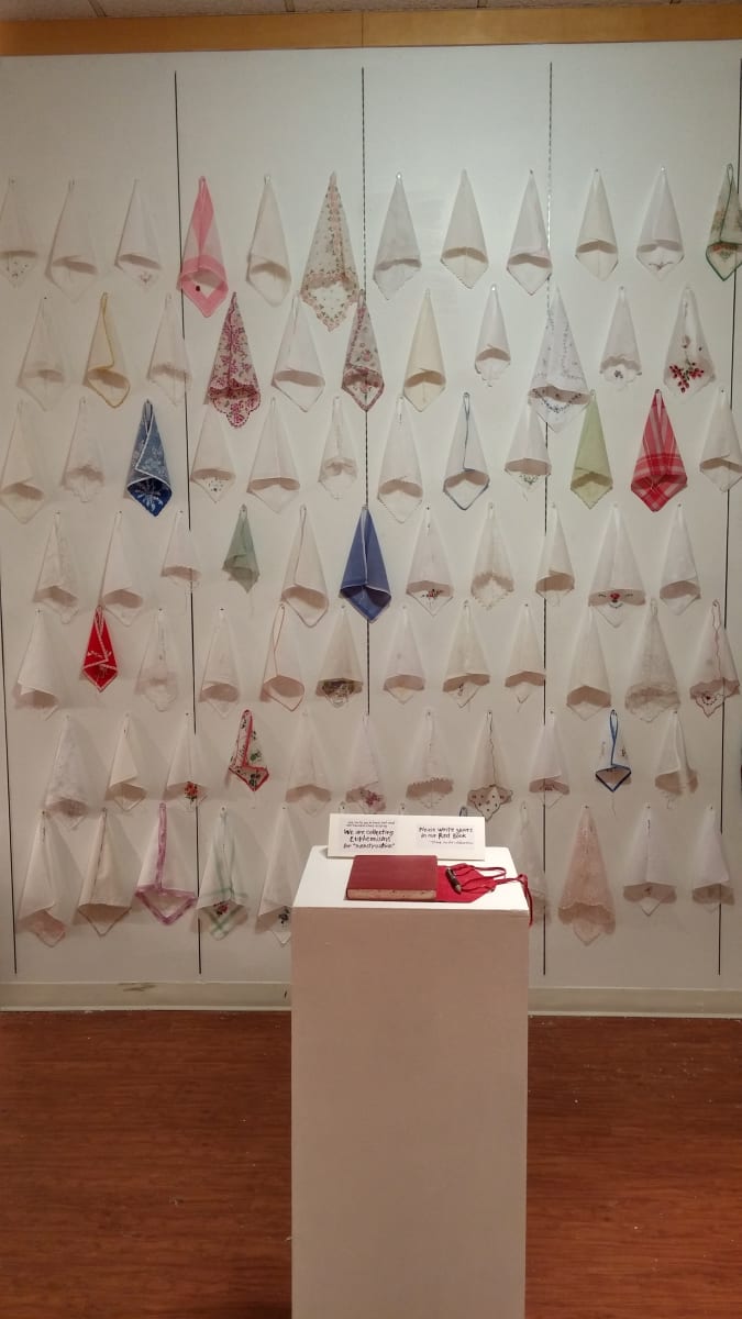 Aunt Flow Speaks Out by Lesley Turner  Image: Lesley Turner, 'Aunt Flow Speaks Out', 2014, 120"h x 45"w x 180"d - variable. Cotton, linen, and silk handkerchiefs installed on the wall with a plinth holding a book and pen. 