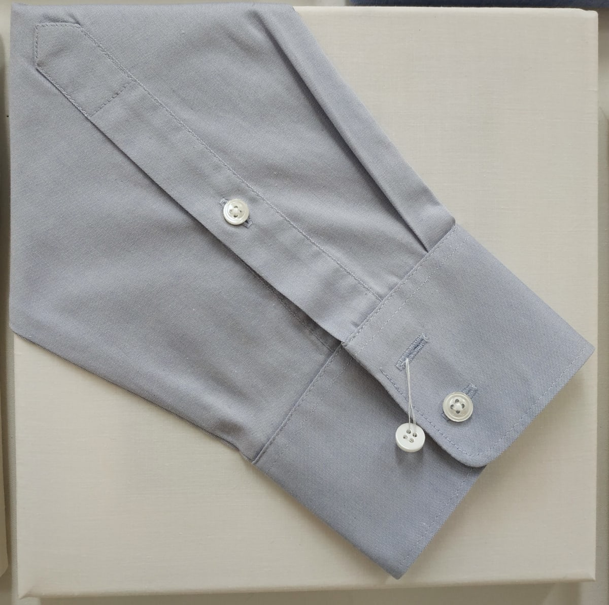 Idiom: Off the Cuff by Lesley Turner  Image: Lesley Turner, 'Idiom: Off the Cuff', 2020, 9"x9". Cotton shirt cuff, plastic buttons, cotton bedsheet, polyester thread. An off-the-cuff comment is made without being prepared or thought of in advance. 