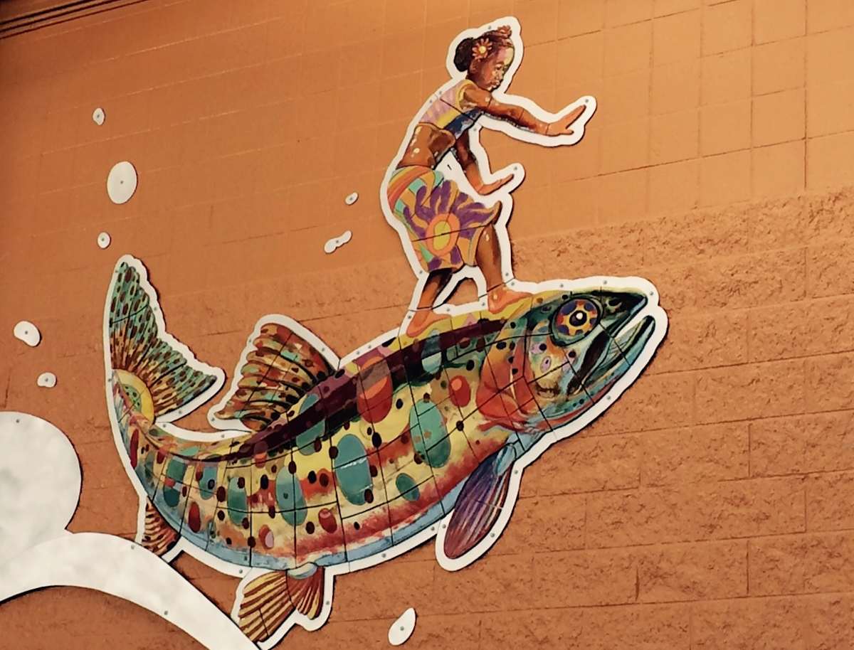 Somewhere Down the Lazy River (Permanent Public Art) by Mario Miguel Echevarria  Image: In 2015, artist Mario Miguel Echevarria won a commission to create a piece of public art for the Parker Recreation Center’s new indoor leisure pool. Inspired by kids’ love of animals and a desire to celebrate Colorado’s native aquatic species, Echevarria created a three-part piece in which “kid power” is amplified by the uniquely amazing skills of Colorado’s river and lake inhabitants. You’ll discover a boy flying with a Painted Turtle, a girl surfing with a Cutthroat Trout, and a girl riding on a Clark’s Grebe. Each work is crafted from ceramic tile and aluminum sheeting. As Echevarria says, “When people see a kid surfing on a fish the size of a VW Bug, they will never look at a trout the same way again!”