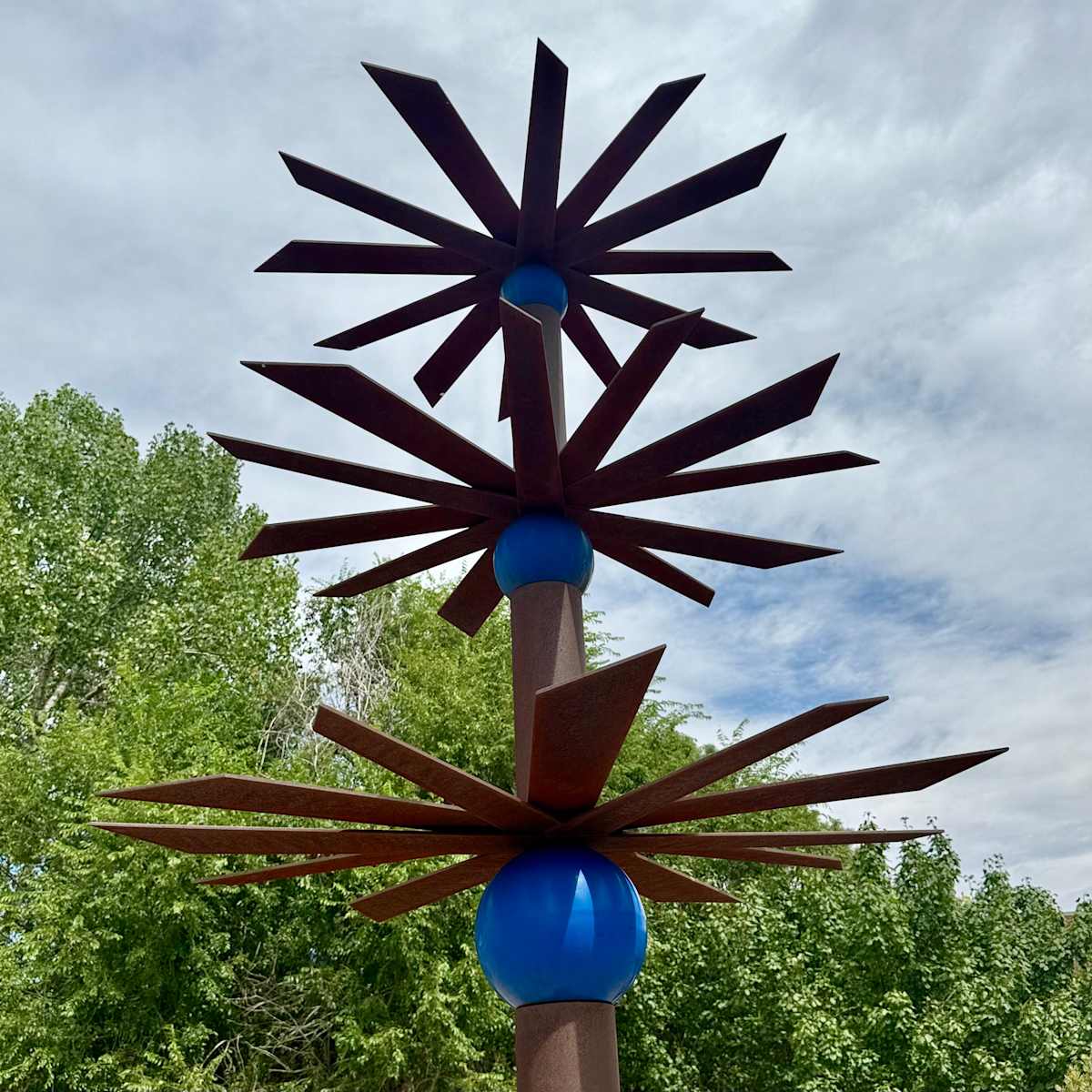 I'm Dreaming With My Brain Awake (Permanent Public Art) by Sandy Friedman  Image: “I’m Dreaming With My Brain Awake” is a steel and powder coated sculpture by artist Sandy Friedman, whose work is influenced significantly by the environments of Colorado and the Southwest. 
In this sculpture, the colored spheres are depicting Father Sky, and the slightly patinated horizontals, along with the columns, represent Mother Earth. The horizontals also indicate the vastness of the land as seen in all directions, and the columns are the strength of the Earth and represent the mountains.