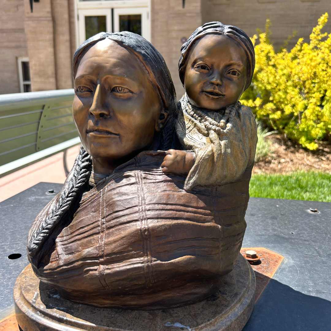 Sioux Mother and Child (Art Encounters 2024) by Garry Carlson  Image: Artist Garry Carlson’s bronze sculpture, “Sioux Mother and Child,” was inspired by historical and cultural narratives surrounding the strength of women and maternal bonds within the Native American community. The weight and stature of bronze, he says, echoes their resilience despite hardship. “The sturdiness of the bronze medium paired with the gentle depiction of familial love seeks to reflect the resilience and tenderness inherent within these narratives.”