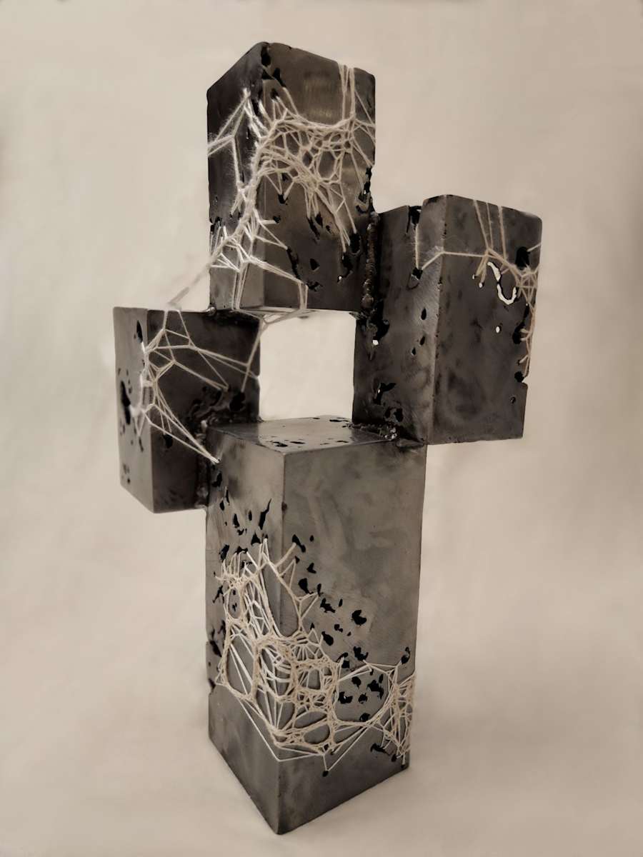 Growth via Decay by Amanda Langer  Image: Four rectangular steel prisms arranged vertically. Holes populate the surface of the steel, polished smooth. Crocheted fiber attaches to the holes and stretches over the surface. 