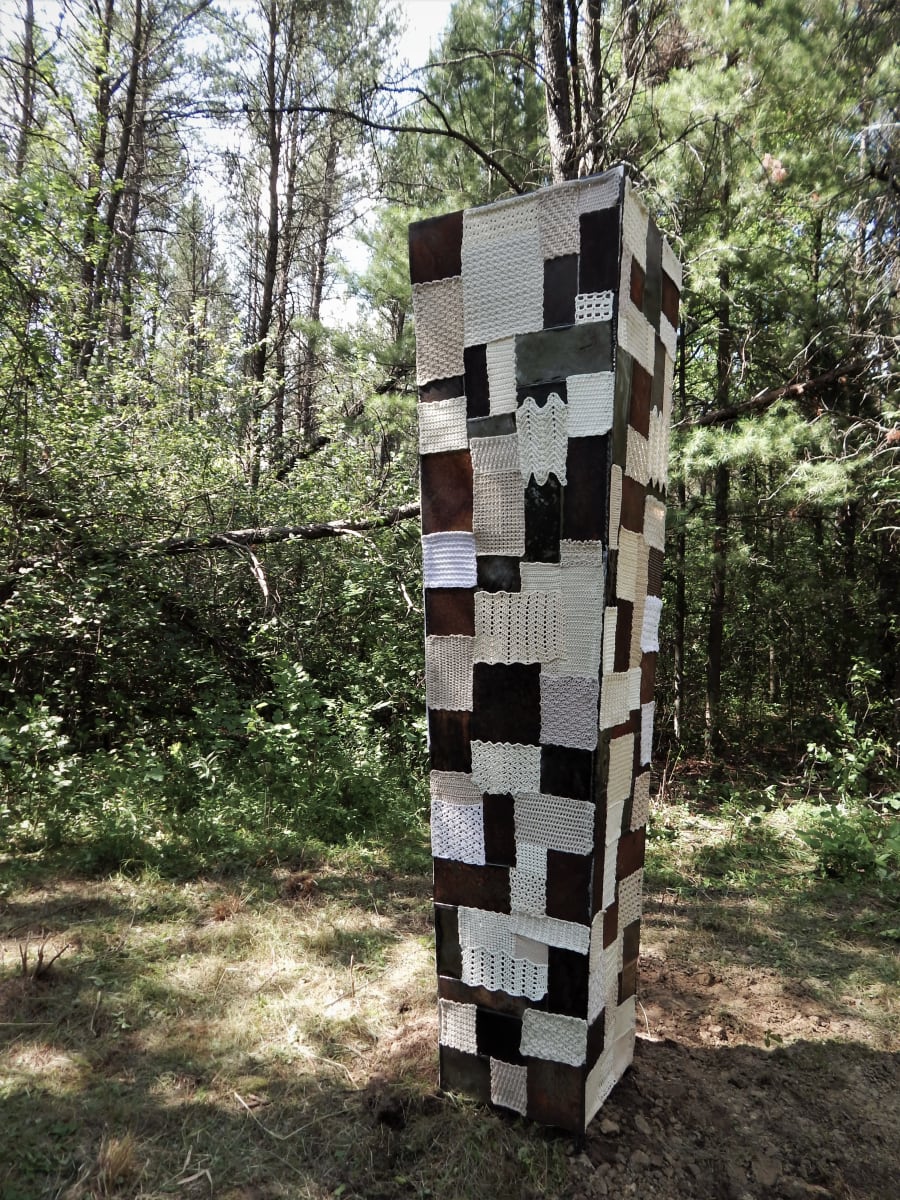 Fabricated by Amanda Langer  Image: 8 foot tall steel sculpture. Surface is quilt-like pattern of steel and fiber rectangular pieces. Variety of finishes, textures, and patterns of pieces. 