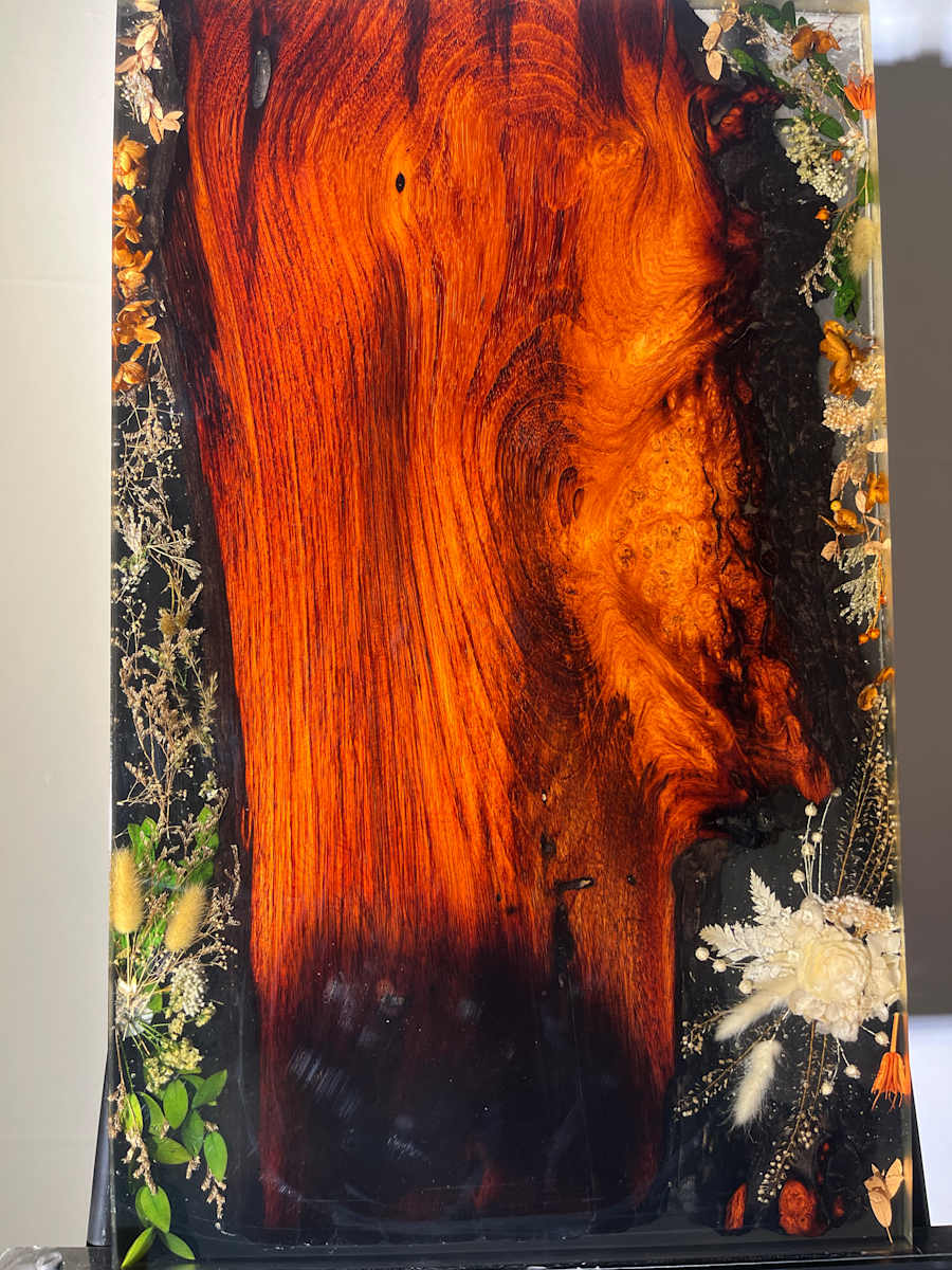 Sai Fai — “Charred Flame Edge” by Martin Halpin (Mandara)  Image: This reclaimed redwood slab holds fire in its grain and shadow in its shape. Native blossoms rise from a jet-black resin void, where one end is scorched — a burnt edge that speaks of time, resilience, and the quiet mystery of transformation.