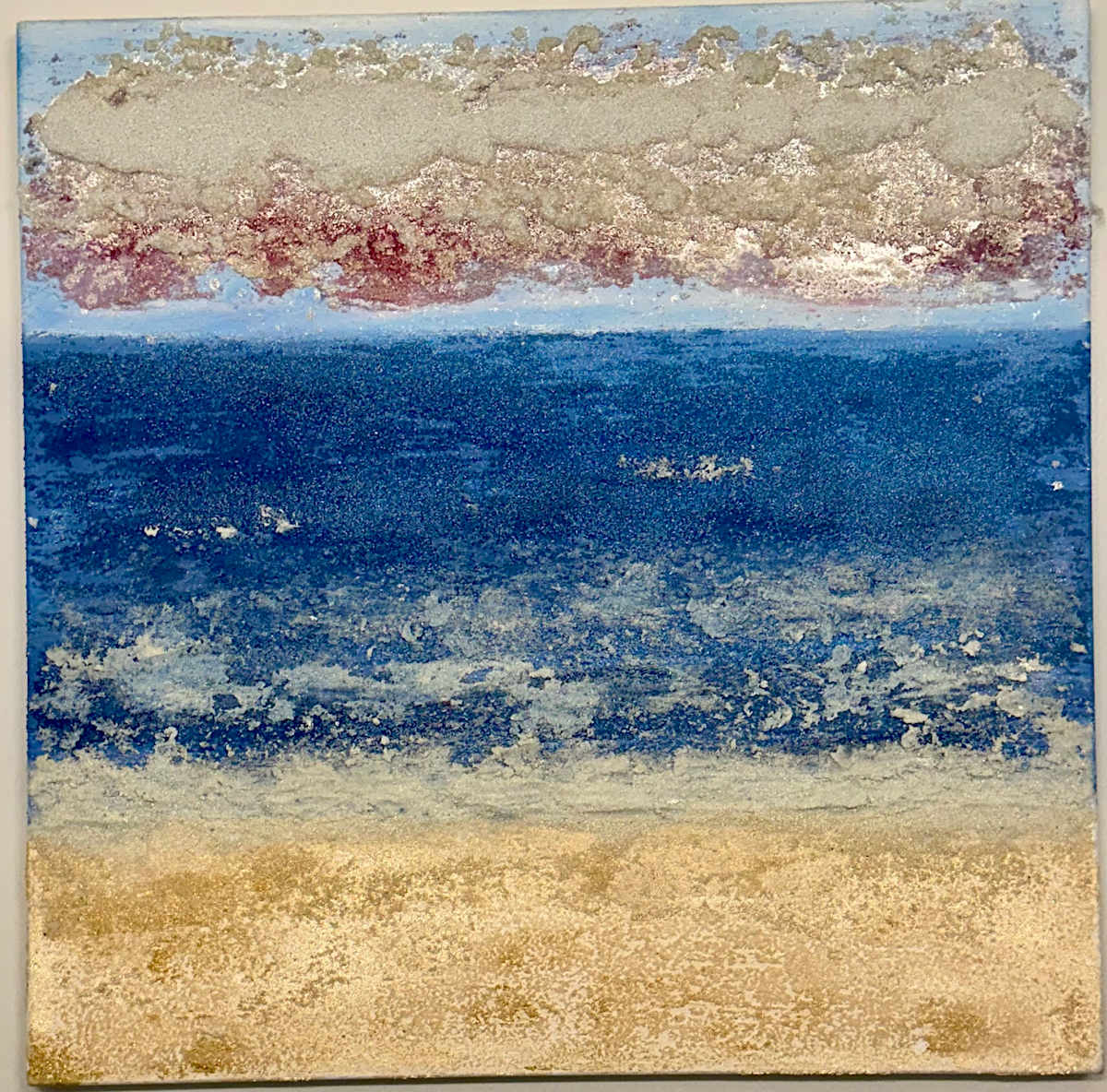 The Gilded Tide’s Veil by Peter Studl  Image: "The Gilded Tide’s Veil" is a vibrant, 36x36 unframed immersive capture of the coast’s most atmospheric hour. At its foundation lies a gilded expanse of shore, where the silica creates a tactile, sun-drenched grit that feels warm to the eye. Above, the deep cerulean ocean surges, its movement rendered in crystalline white froth that seems to hiss against the sand. The piece is crowned by a heavy, ethereal band of silica clouds that float with a mysterious weight, blushing with soft magenta and silver undertones. This work masterfully bridges the gap between the solid earth and the spray of the sea, inviting the viewer into a world of salt-kissed light and ancient, rhythmic peace.