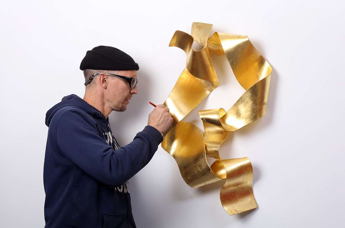 sculptor Stefan Duerst applying gold leaf to his wall sculpture