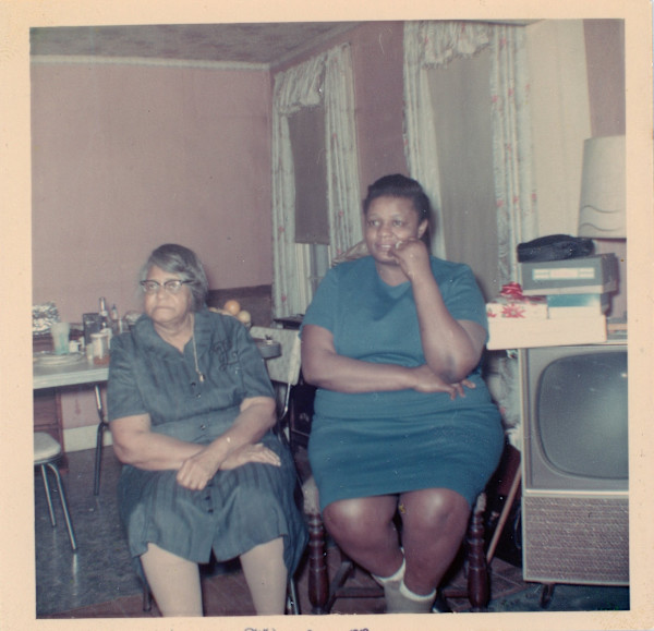 Two women sitting in pink room; one with rolled hosiery by Unknown