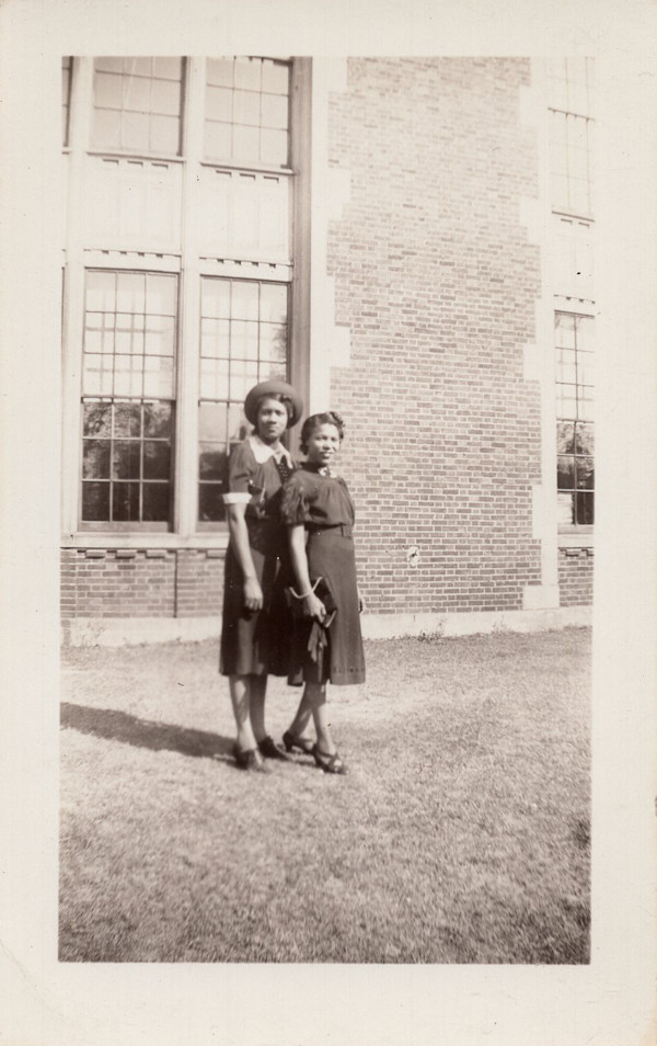 Two women in dark dresses outside brick building by Unknown