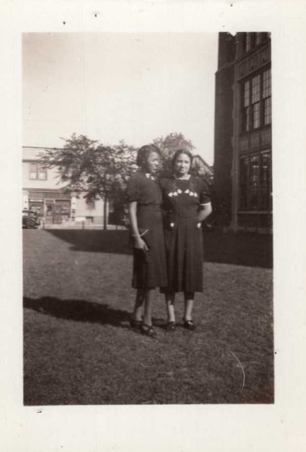 Two women in dark dresses outside brick building by Unknown