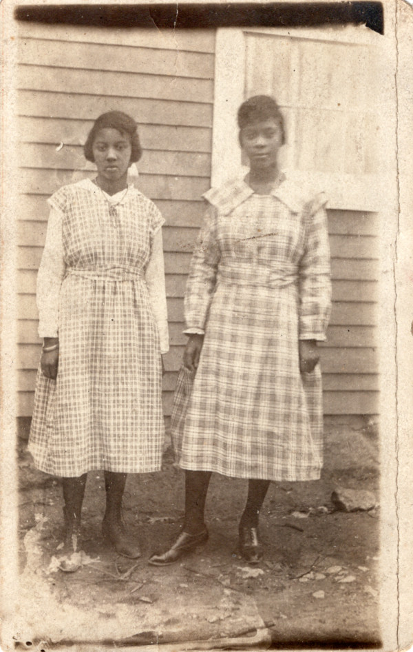 Two women in plaid dresses on side of house by Unknown
