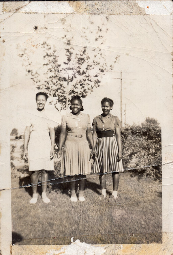 Three women in midi skirts standing in yard by Unknown